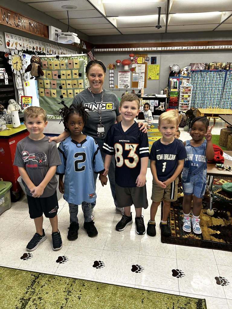 Five students stand with teacher sporting their favorite team logos on their shirts