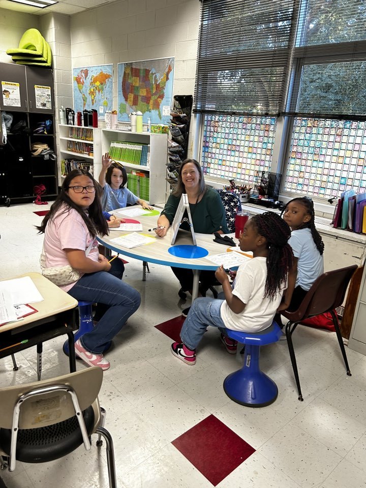 teacher sitting with group of students at kidney shaped table teaching