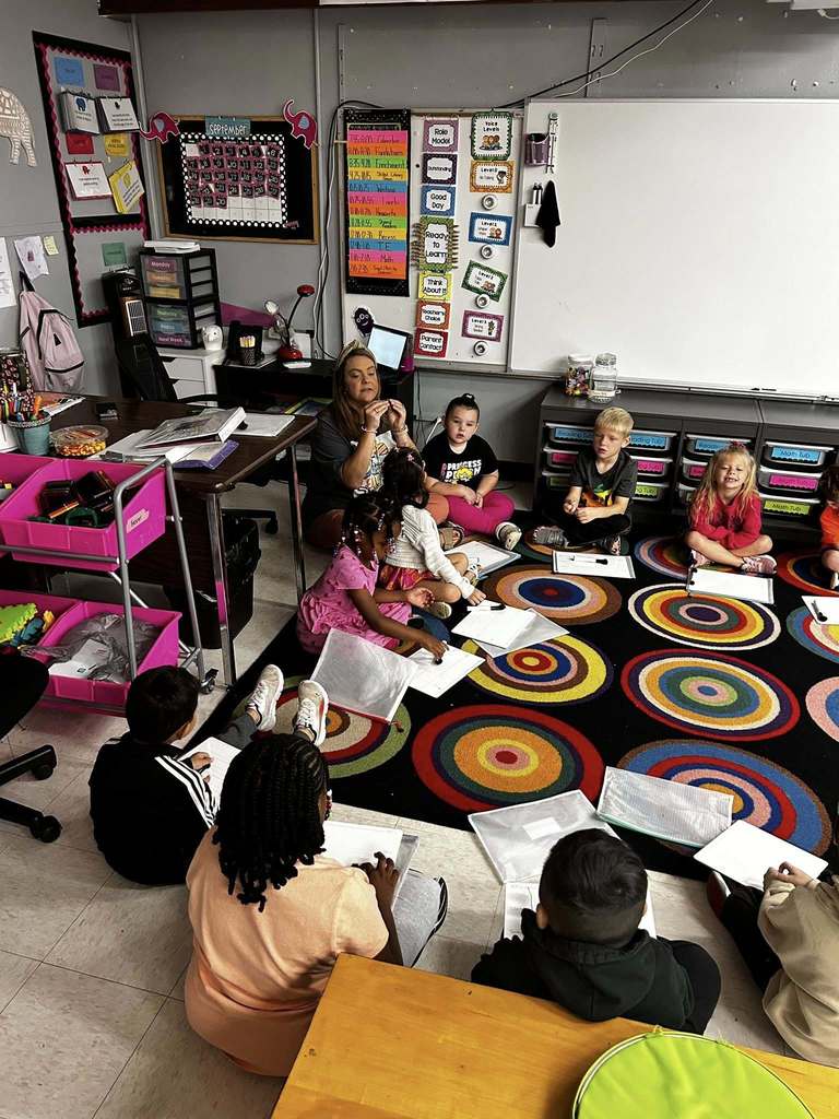 teacher sitting on carpet with class teaching