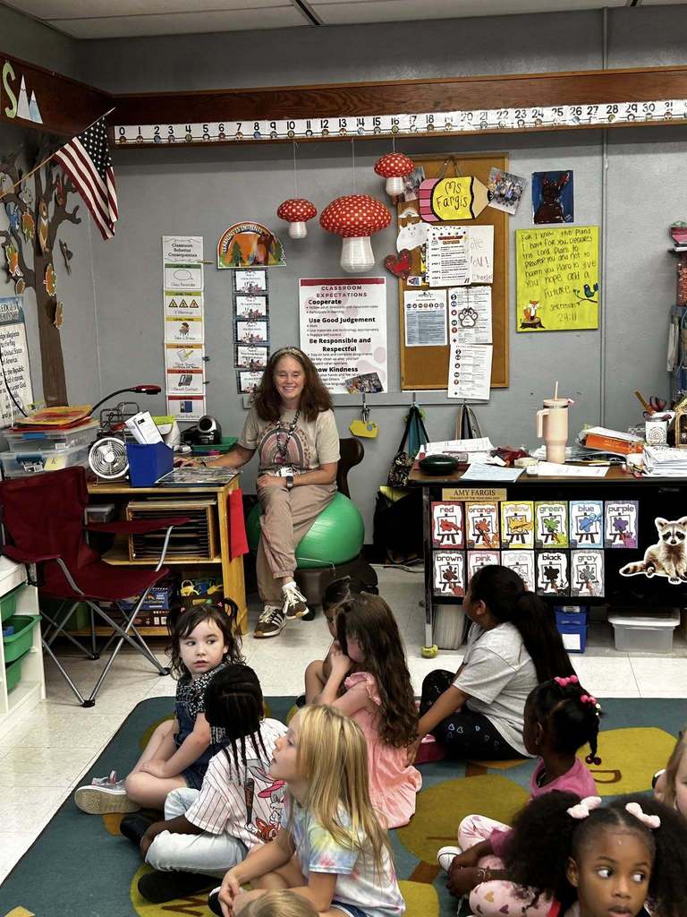 teacher sitting at front of room teaching students