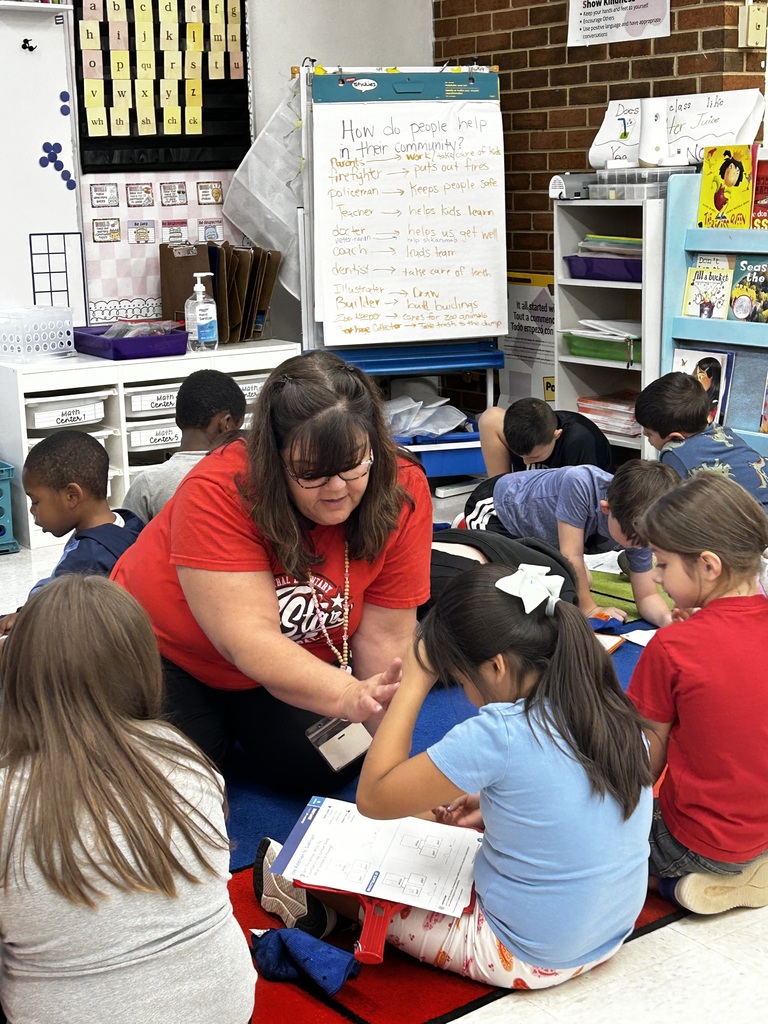 A teacher works on the carpet with a group of students who are working on a worksheet