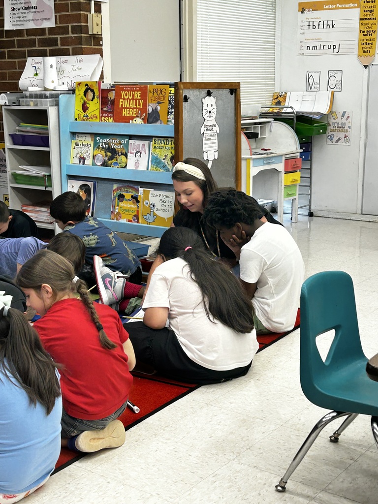 A teacher works on the carpet with a group of students.