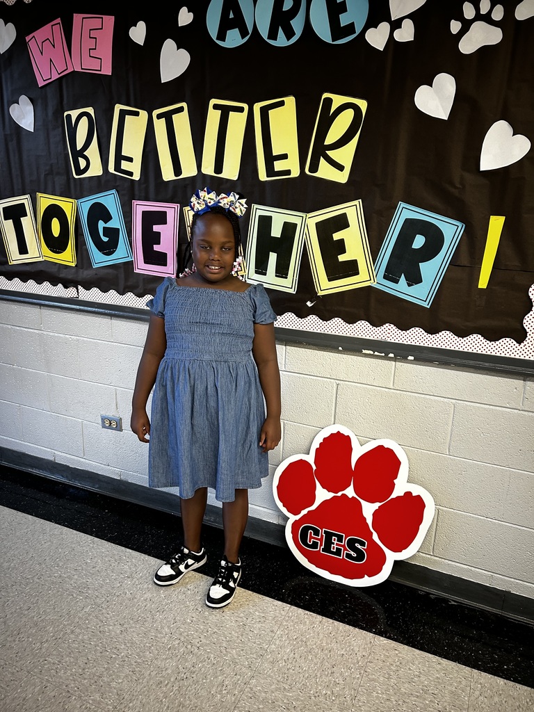 A black girl stands in front of a bulletin board. She's beside a large red paw with the letters CES on it.