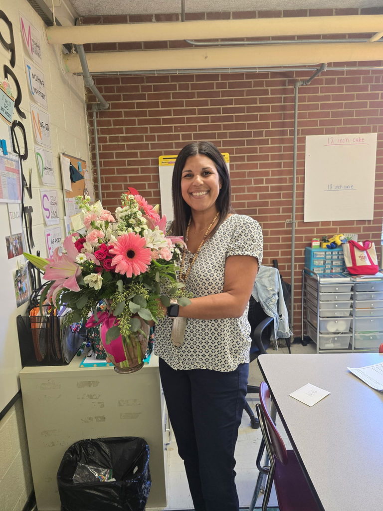 Instructional coach stands in her classroom holding a large bouqet of flowers from a florist.