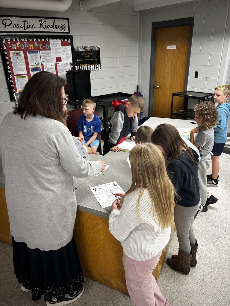 teacher stands at desk with a group of students working on worksheet