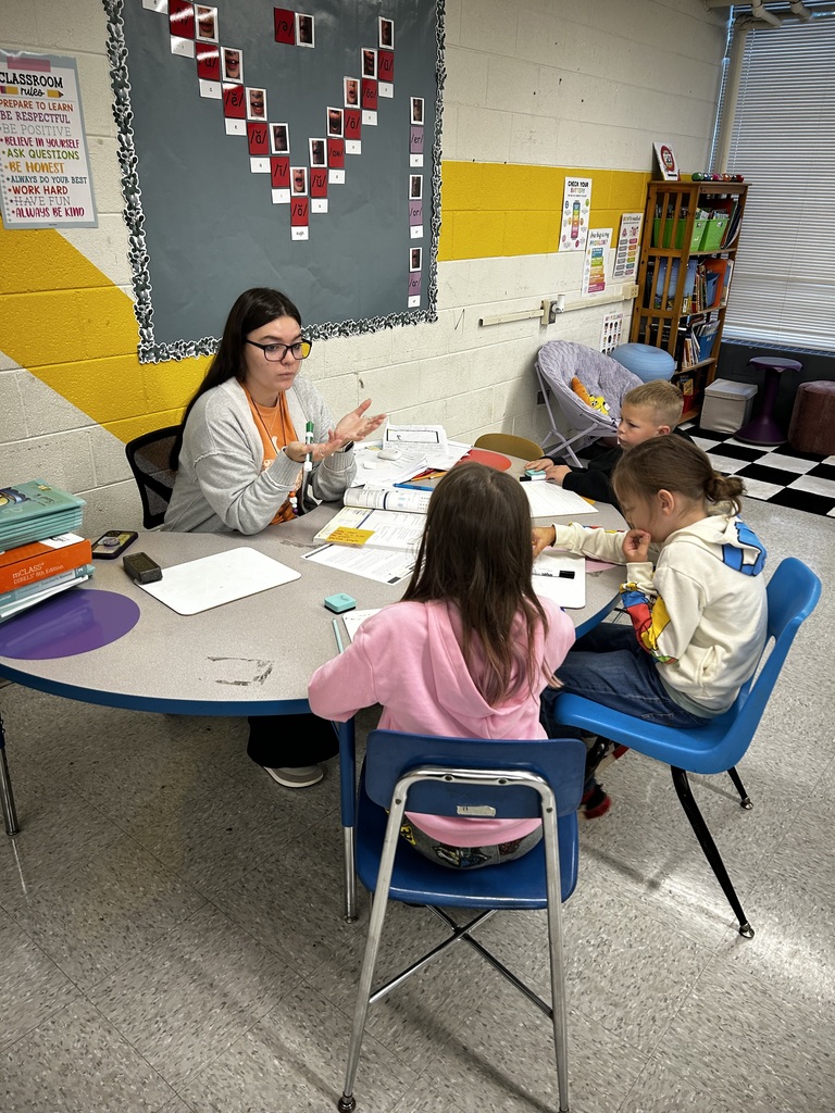 teacher sits at kidney table with three students