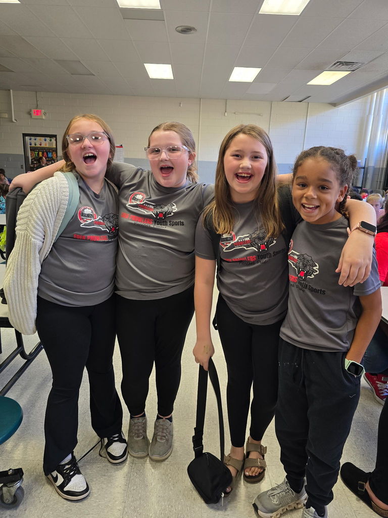 Four girls stand with arms around each other wearing matching gray shirts and black leggings. 