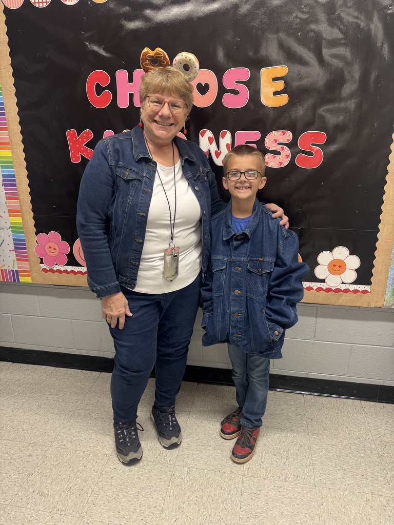 a teacher stands with a student. Both are wearing blue jeans and denim jackets. 