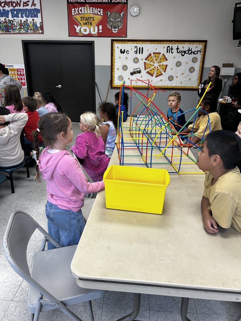 Students sit together at table building a structure. 