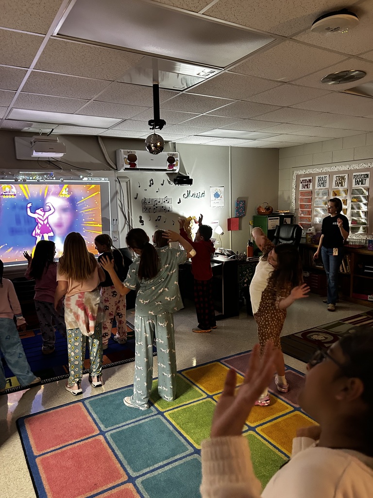 Students stand in dark room with dance game on active board.