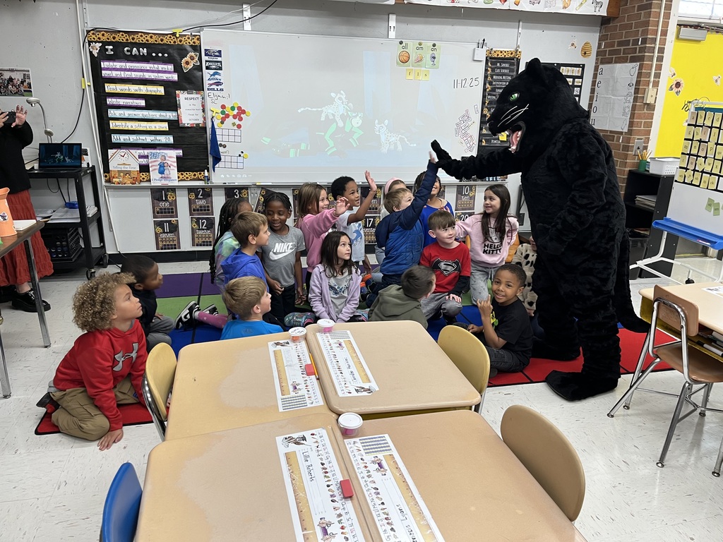 The black panther cub mascot is seen giving high fives to students as they sit on the classroom carpet. 