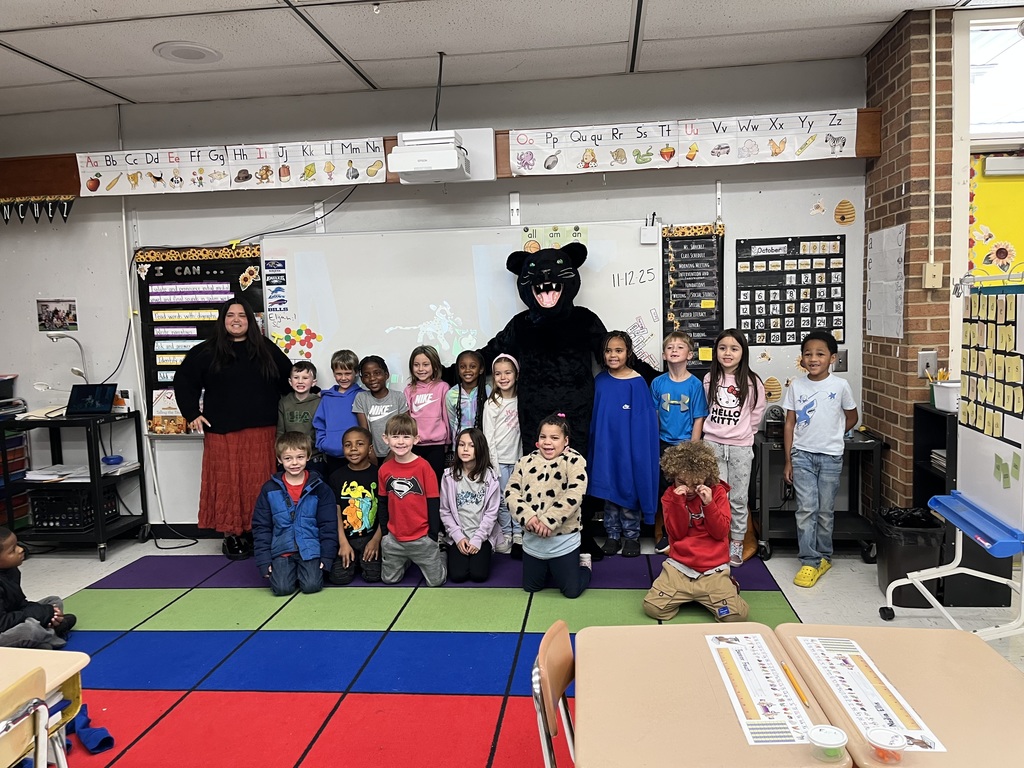 Students and teacher stand at the front of the room with black panther cub mascot. 