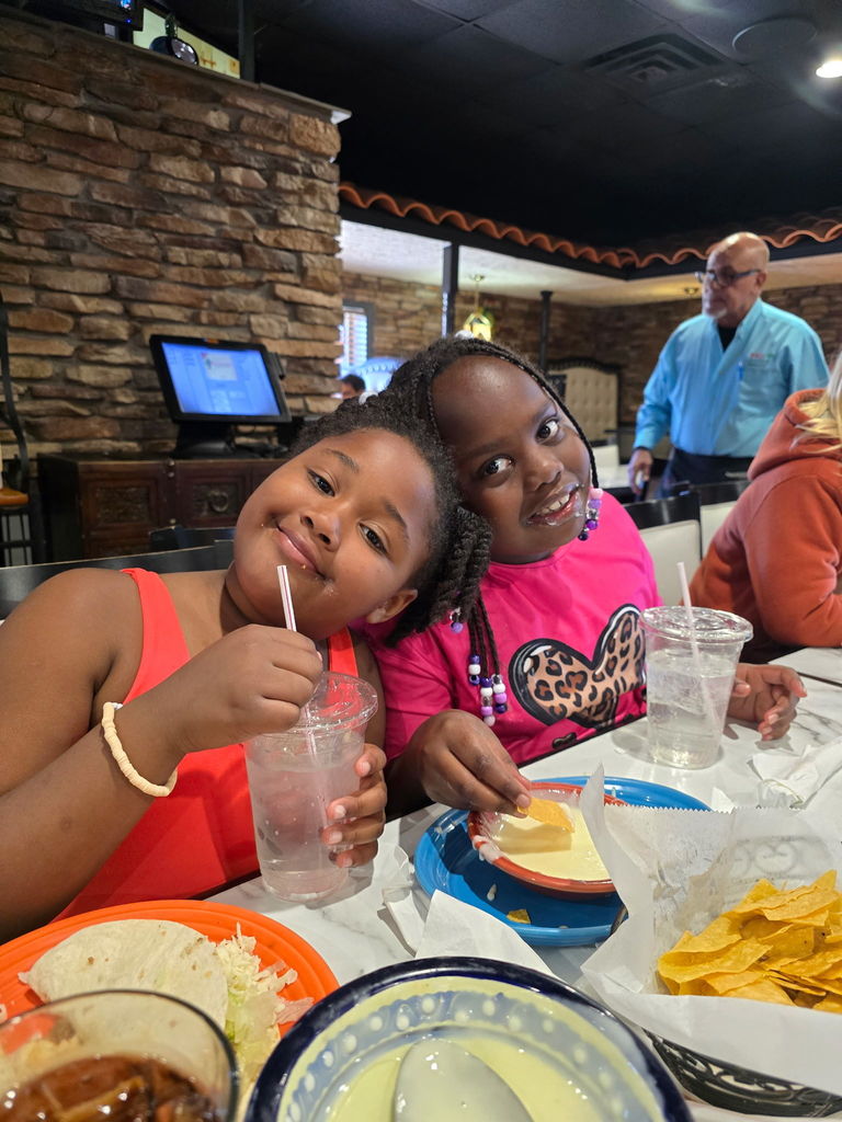 Two students lean on each other as they sit at a table