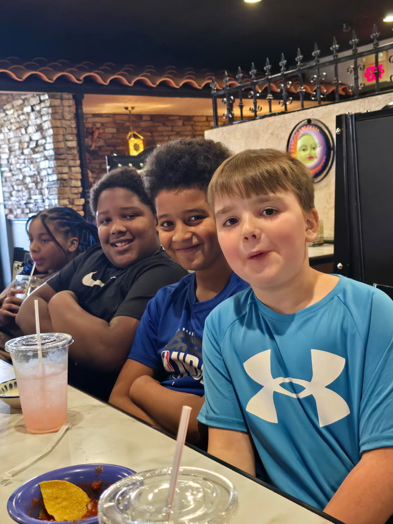 three boys smile together while sitting at table in restaurant 