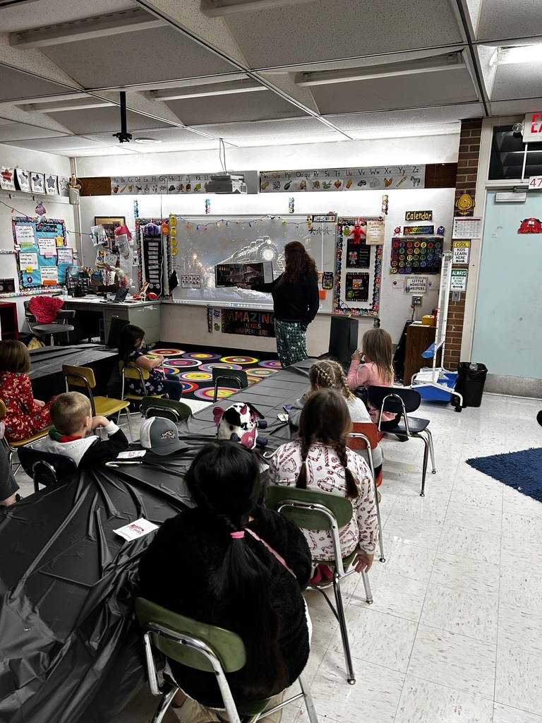 Teacher stands at the front of the room and reads a story while students sit in chairs listening