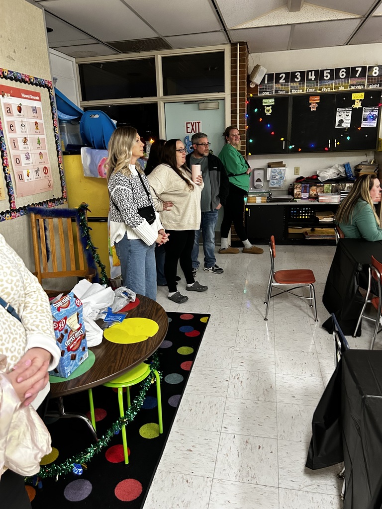 four parents stand at the back of a classroom listening to a story