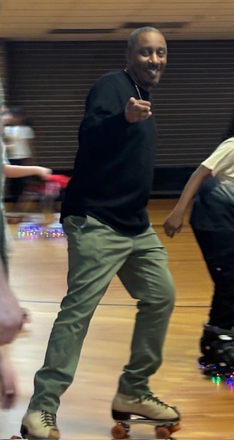 .Assistant principal wearing skates and rolling across the rink at PTA Skate Night while students skate nearby and families watch from the sidelines.