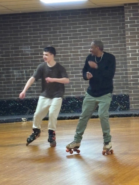 Assistant principal skating on a roller rink floor during the school’s PTA Skate Night, smiling and interacting with students under colorful rink lights.