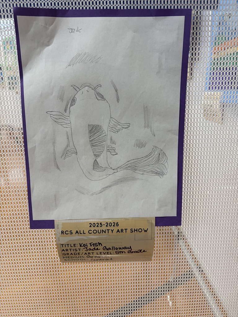 A 5th grade student artwork titled "Koi Fish" by Jade Galloway is displayed as part of the 2025-2026 RCS All County Art Show from Central Elementary School. Created with graphite pencil on white paper, the drawing depicts a koi fish with visible fins and a detailed tail. The fish's body features shading and detail work, with background lines suggesting water. The artwork is matted with purple paper and affixed to a white mesh display surface.