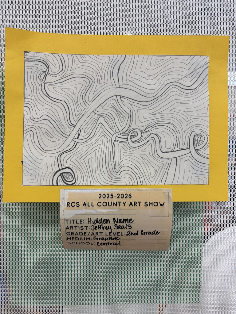 A 2nd grade student artwork titled "Hidden Name" by Jeffrey Seals is displayed as part of the 2025-2026 RCS All County Art Show from Central Elementary School. Created with graphite on white paper, the drawing features a dense pattern of black lines varying in thickness. Some lines form large, flowing, interconnected shapes that could be interpreted as stylized, abstract text representing a hidden name, while others create a background of wavy, topographical map-like contours. The drawing is framed by a yellow border and displayed against a white mesh background.