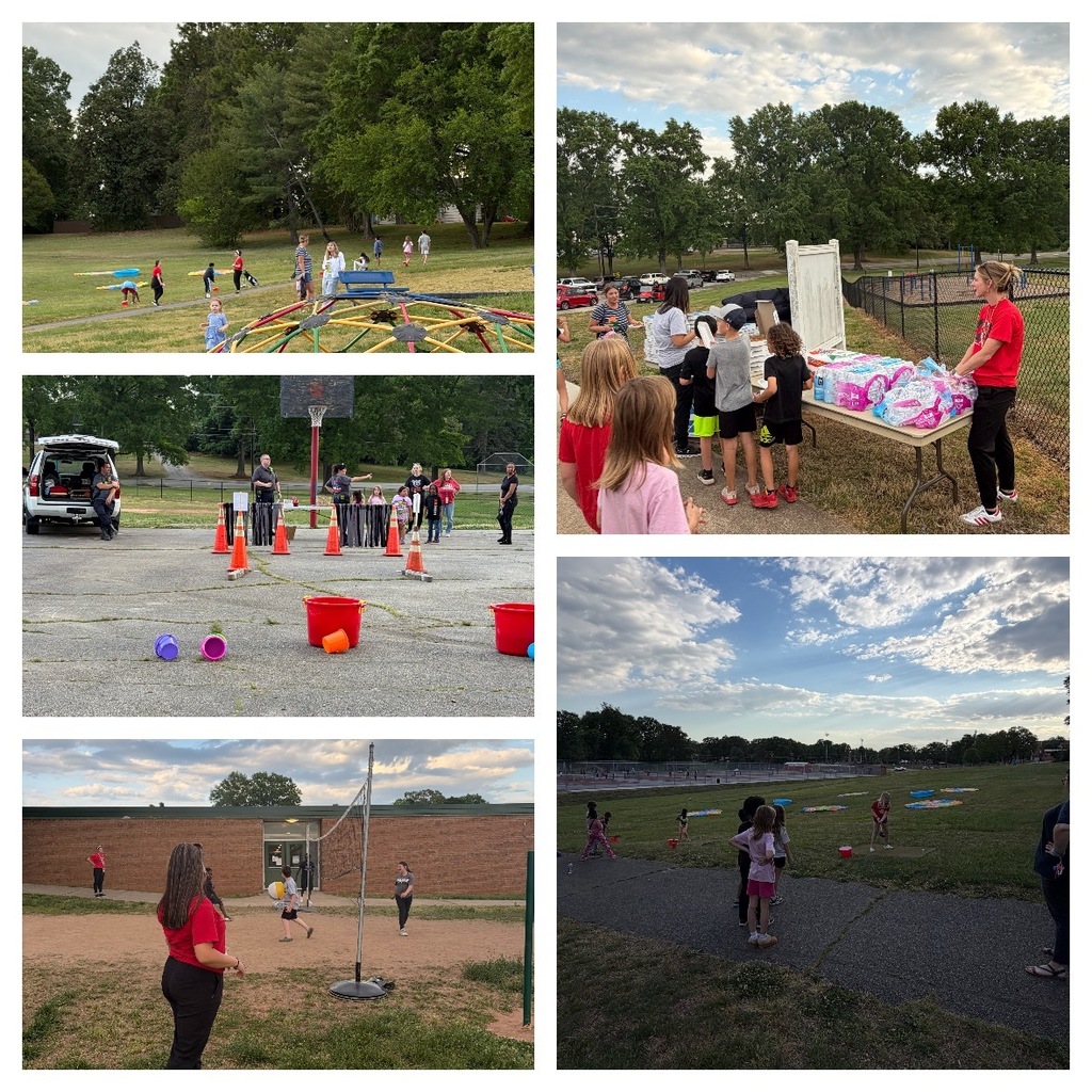 Students and families enjoy outdoor activities on a grassy field during a school event. Children play games and explore activity stations spread across the lawn. A line of students gathers at a table where staff distribute supplies. In a parking lot area, cones and buckets are set up for a game while adults supervise. Students play volleyball near a school building, and others participate in field games under a partly cloudy sky.