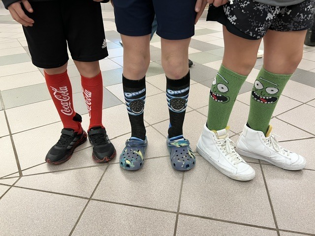 Red Ribbon Week- Monroeton Elementary crazy sock day: left to right, red knee-high Coca-Cola socks, black knee-high Oreo socks with a white and blue logo, green "Pickle Rick" knee-high socks