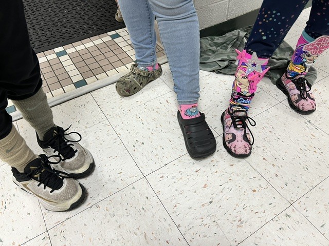 Red Ribbon Week- Monroeton Elementary crazy sock day: left to right, student in mixed-matched Nike socks, student in pink socks with a blue character on them, student in K-Pop Demon Hunters socks that are knee-high