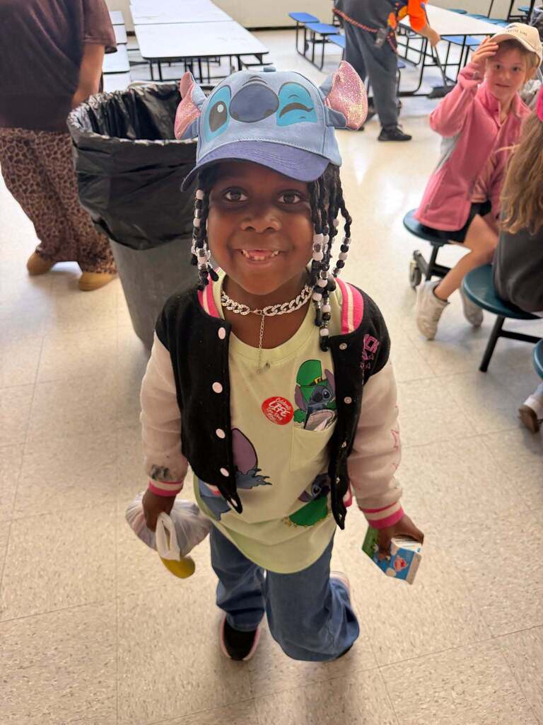 Red Ribbon Week- Central Elementary Hat Day: Little girl smiling and posing for a picture in the cafeteria while wearing a blue "Stitch" hat