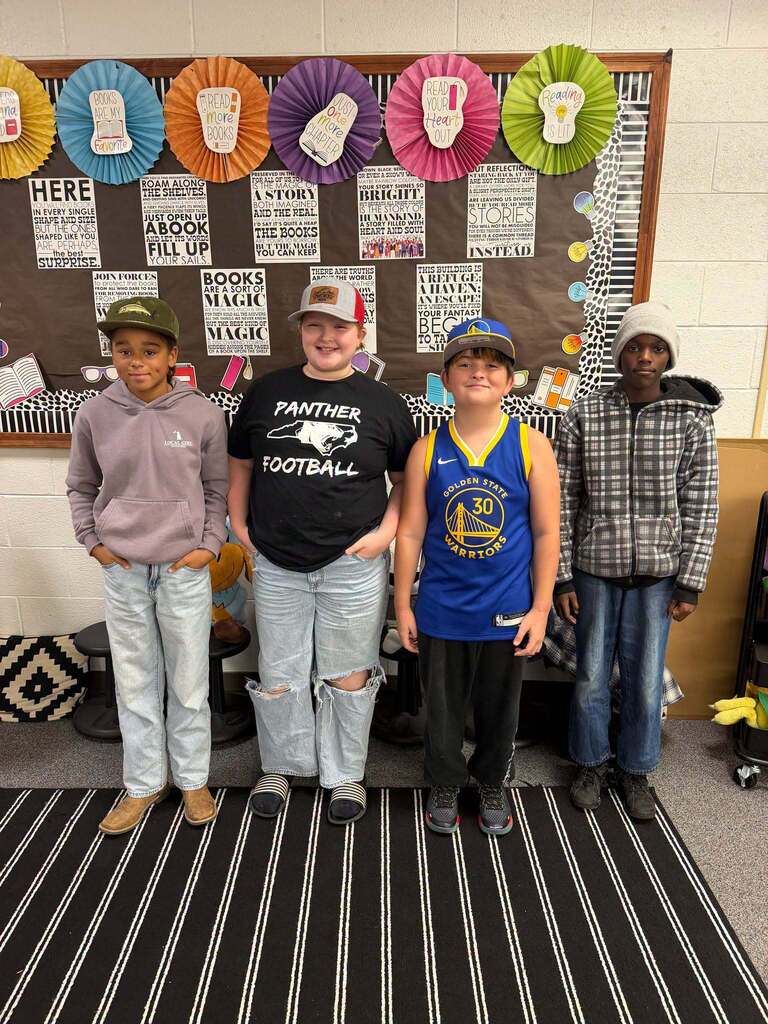 Red Ribbon Week- Central Elementary Hat Day: 4 young boy students. Left is wearing an olive green hat with a yellow symbol, left middle is wearing a white and red hat, right middle is wearing a blue and yellow hat and right is wearing a white beanie