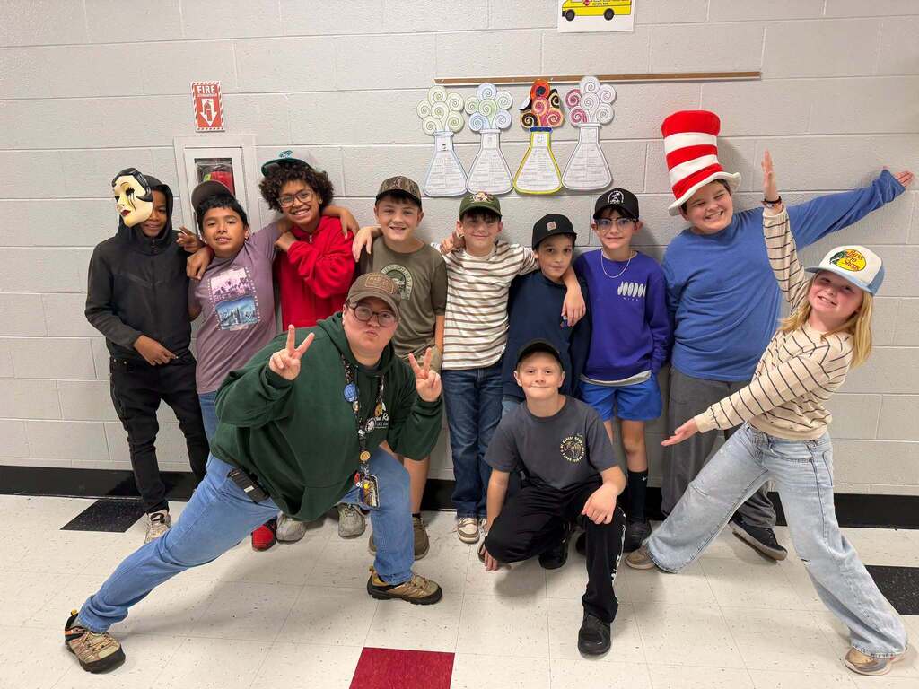 Red Ribbon Week- Central Elementary Hat Day: A teacher posing with 10 students in their school hallway. All are wearing various style hats