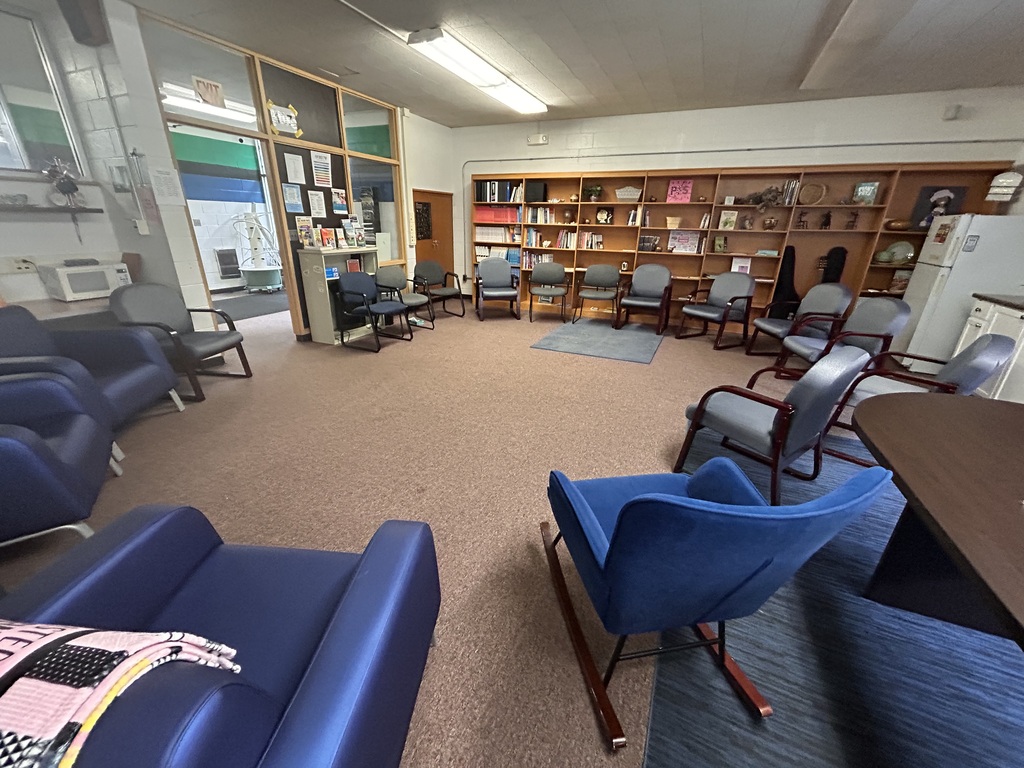 A waiting room with blue chairs, a blue table, and a wooden shelf filled with books.