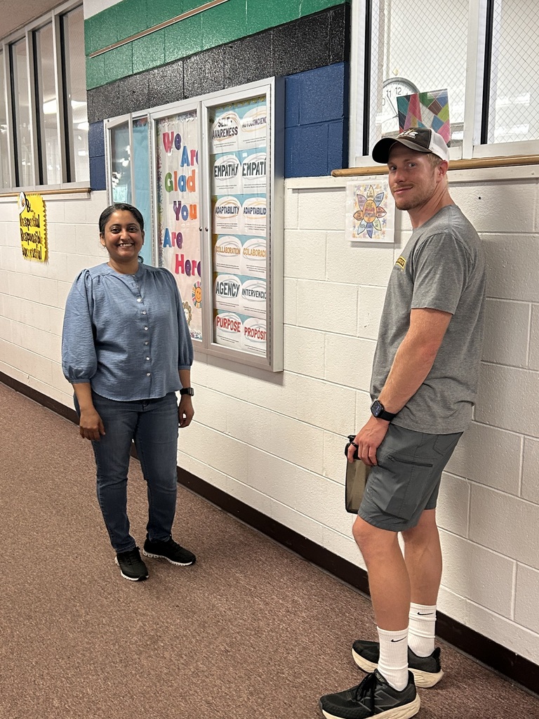 Two people in a school hallway. A man in gray shorts, and a woman in blue jeans.