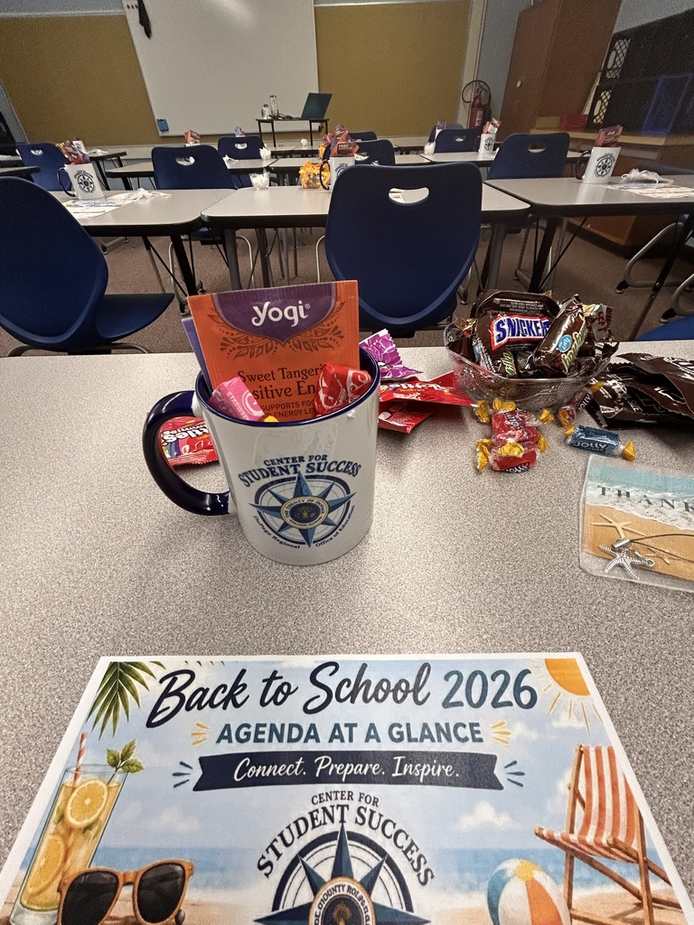 A table with a cup full of candy, a brochure, and a book titled "Back to School 2026" in a classroom setting.