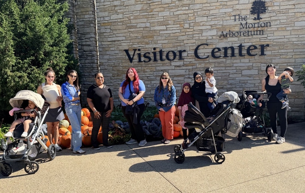 A group of people stands outside The Morton Arboretum Visitor Center with strollers and pumpkins.
