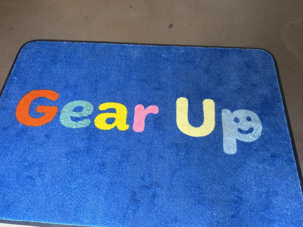 Blue carpet with "Gear Up" written in colorful letters and a small smiley face.