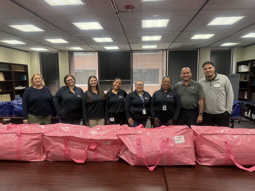 A group of people stands behind large pink bags in an indoor office setting with large windows.