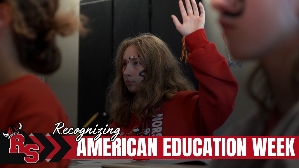 A student wearing red face paint and a red sweatshirt raises her hand during class. Text across the bottom reads, “Recognizing American Education Week,” alongside the Roland-Story school logo.