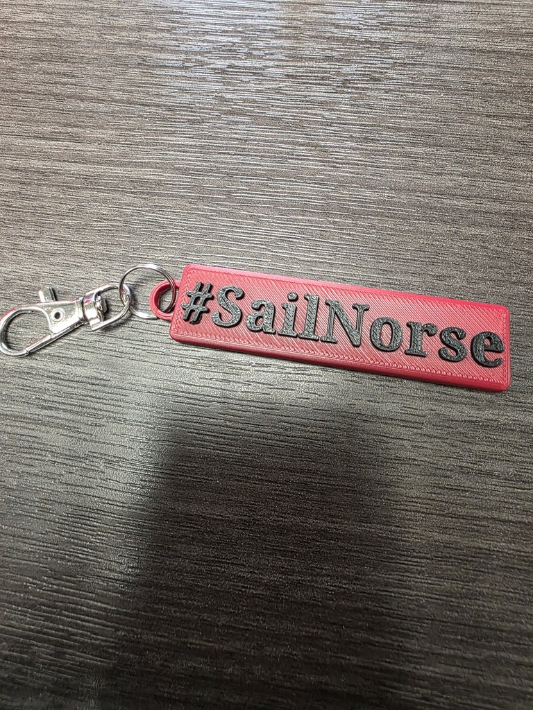 Red keychain with white letters saying "#SailNorse" from our new 3D printers at the MS!