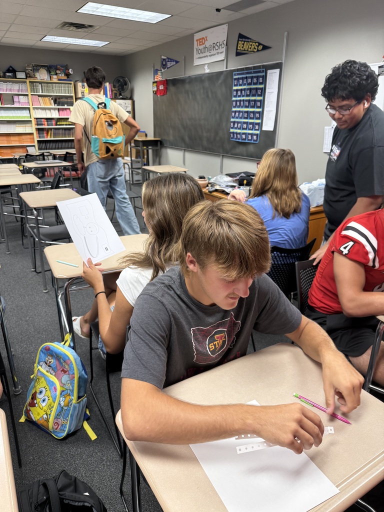 Several students are seated at desks in a classroom, one student is focused on paper work.
