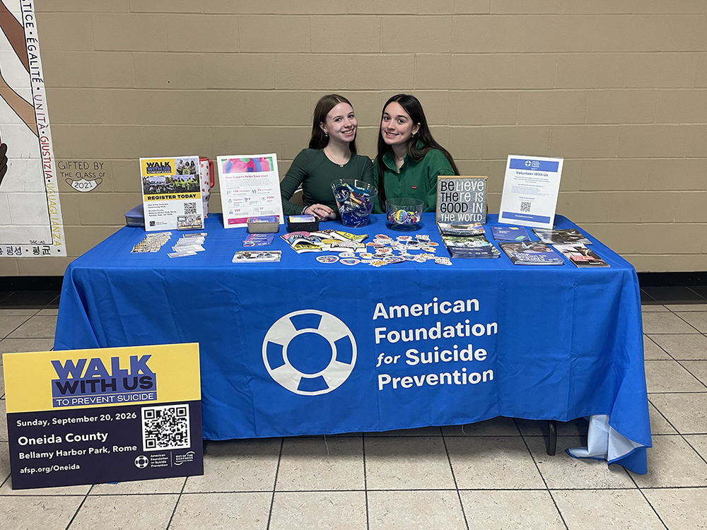 Two students pose for a photo while sitting at a table.