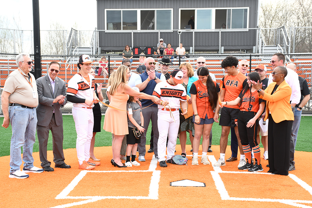 Team captains from the Rome Free Academy baseball, softball, and tennis teams cut the ribbon at home plate of the new RFA baseball field while being joined in celebration by Rome City School District staff and Rome community leaders.