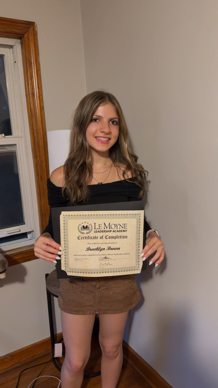 A student smiles for a photo while holding their Leadership Academy certificate.