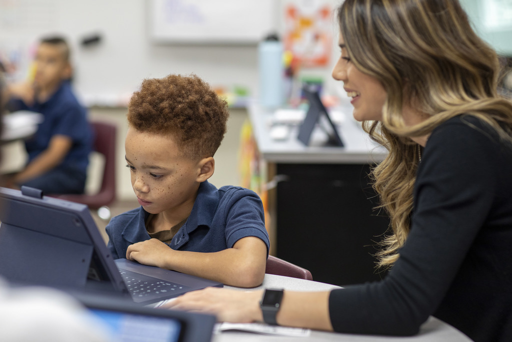 A teacher sitting with a student working on an iPad