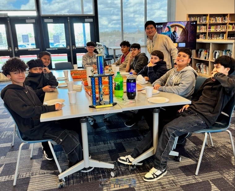 Male boys esports team esting pizza around a table with their blue trophy in the middle of the table