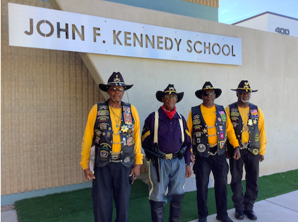 4 Buffalo Soldiers wearing their military medals, standing in front of John F. Kennedy sign