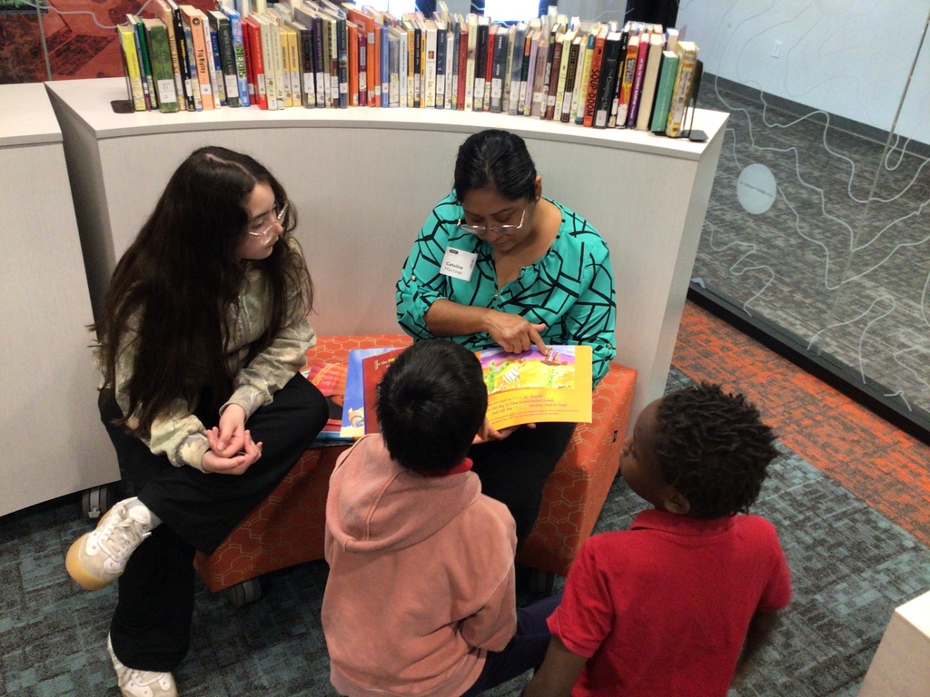 A lady wearing a green blouse is reading to 3 students.