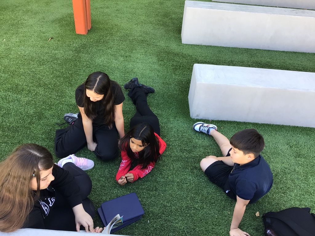 A student is reading to 3 younger students while sitting in the grass.