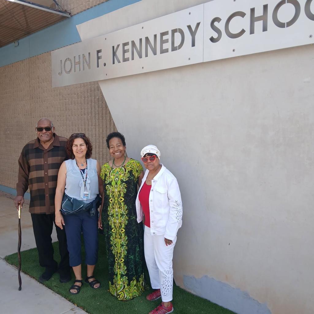 4 adults standing in front of the John F. Kennedy sign.