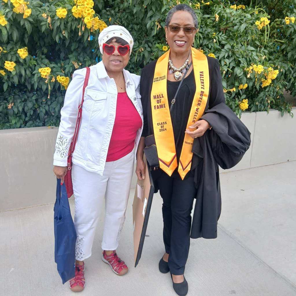 2 lady volunteer readers standing in front of blooming yellow flowers.