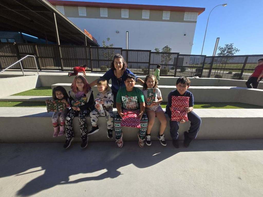 Adult female standing behind 6 students sitting on concrete bench outside.
